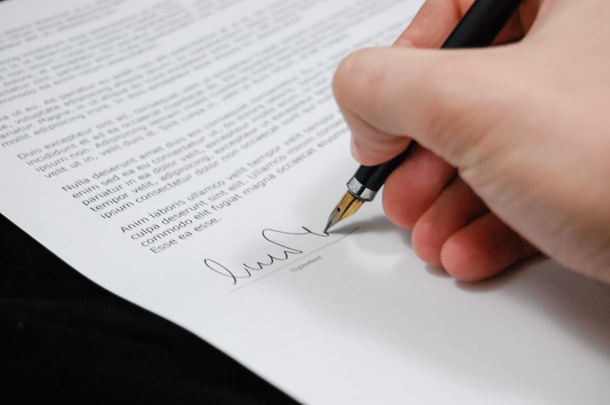 Mano firmando documento legal con bolígrafo, símbolo de acuerdo de póliza